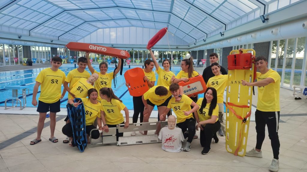 Grupo de alumnos posando en la piscina con materiales de rescate durante el curso de socorrismo acuático.